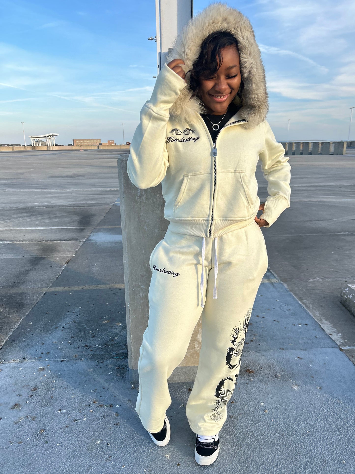 Person wearing a white hoodie and pants with a hood, standing on a concrete surface.